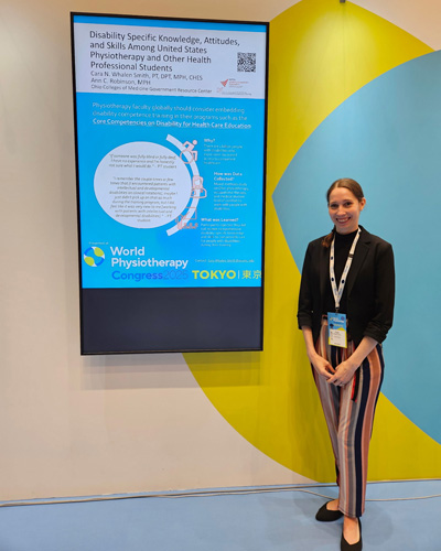 Cara Whalen Smith stands smiling beside a monitor of her presentation 'Disability Specific Knowledge, Attitudes, and Skills Among United States Physiotherapy and Other Health Professional Students.'