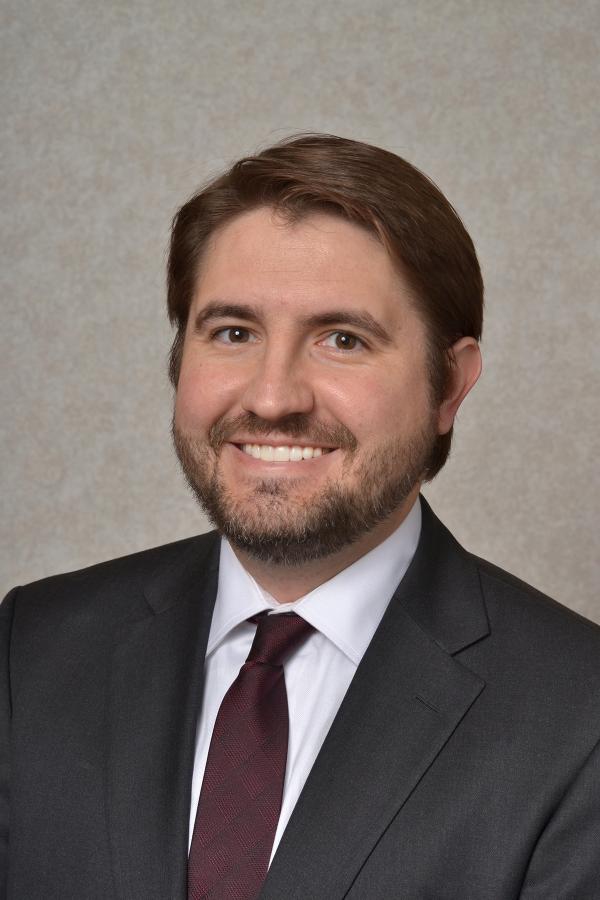 Thomas Albani headshot with suit jacket and dark red tie.